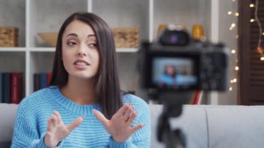 Genç ve çekici esmer kadın kamerayla video blogu kaydediyor. Mutlu kız evde oturuyor ve video kaydediyor..