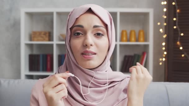 ヒジャーブ州の若く魅力的なムスリム女性は ヘッドセットを使用して自宅で働いています 中東のフリーランスや学生はオンライン会話をしています ロックダウンの概念 — ストック動画