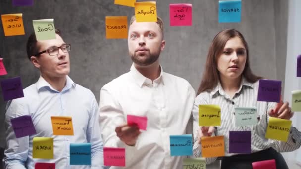 El equipo de empresarios está haciendo una lluvia de ideas en una reunión usando pegatinas en el vidrio. Los trabajadores de oficina están discutiendo estrategia, plan de negocios y metas. Concepto de inicio. — Vídeos de Stock