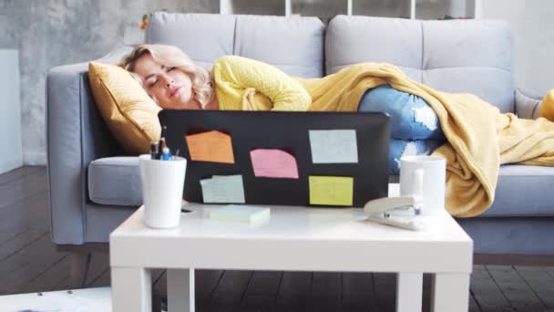 Nezávislá dívka unavená z práce spí ráno na gauči. Žena usnula, když pracovala doma. Uzamčení a koncepce vzdálené úlohy. — Stock video