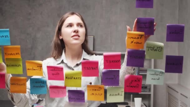 Jonge zakenvrouw brainstormt met stickers op het glas. Kantoormedewerker denkt na over strategie, businessplan en doelstellingen. Startup-concept. — Stockvideo