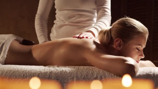 Mulher jovem e bonita recebe terapia de massagem de pedra quente no salão de spa. Estilo de vida saudável e conceito de cuidados com o corpo. — Vídeo de Stock