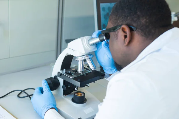 Cientista afro-americano a trabalhar no laboratório. Médico a fazer pesquisa microbiológica. Ferramentas de laboratório: microscópio, tubos de ensaio, equipamento. Biotecnologia, química, bacteriologia, virologia e cuidados de saúde. — Fotografia de Stock