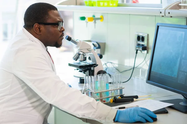 Uomo afro-americano che lavora in laboratorio. Medico scienziato che fa ricerca medica. Strumenti di laboratorio: microscopio, provette, attrezzature. Biotecnologia, chimica, scienza, esperimenti e sanità. — Foto Stock