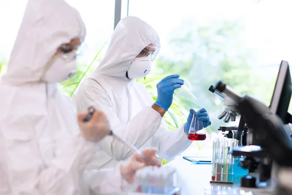 Científicos en trajes de protección y máscaras que trabajan en laboratorios de investigación utilizando equipos de laboratorio: microscopios, tubos de ensayo. —  Fotos de Stock