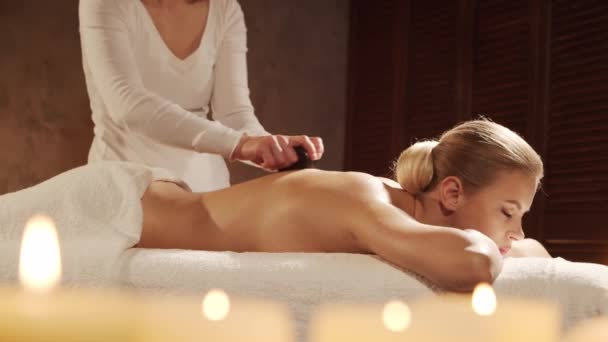 Junge und schöne Frau bekommt Hot Stone Massage-Therapie im Wellness-Salon. Gesunder Lebensstil und Körperpflegekonzept. — Stockvideo