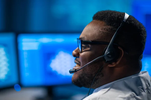 El trabajador del centro de llamadas está hablando con el cliente por auriculares. Lugar de trabajo del operador de apoyo afroamericano. —  Fotos de Stock