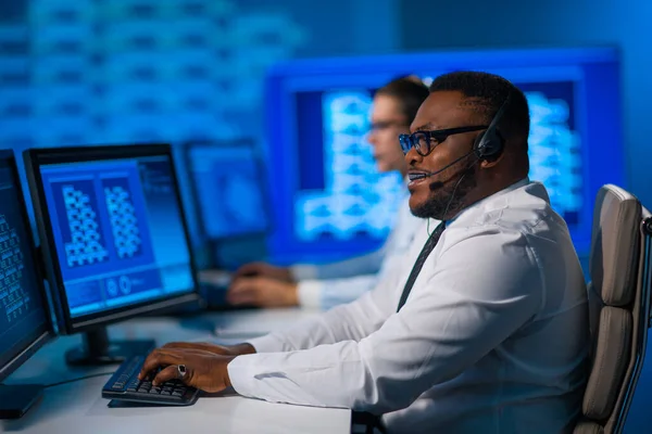 De medewerker van het callcenter spreekt met de klant per headset. Werkplaats van de Afrikaans-Amerikaanse hulpverlener. — Stockfoto