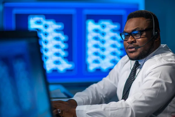 De medewerker van het callcenter spreekt met de klant per headset. Werkplaats van de Afrikaans-Amerikaanse hulpverlener. — Stockfoto