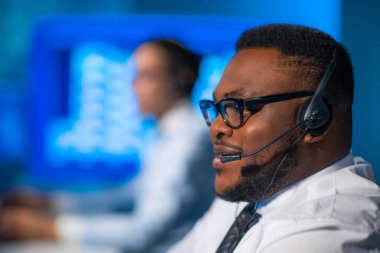 Çağrı merkezi çalışanı müşteriyle kulaklıkla konuşuyor. Afro-Amerikan destek operatörünün işyeri..