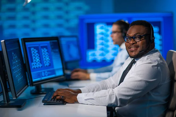 De medewerker van het callcenter spreekt met de klant per headset. Werkplaats van de Afrikaans-Amerikaanse hulpverlener. — Stockfoto