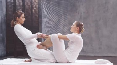 Genç bir kadın terapist tarafından Tayland masajı görüyor. Geleneksel Asya esneme terapisi.