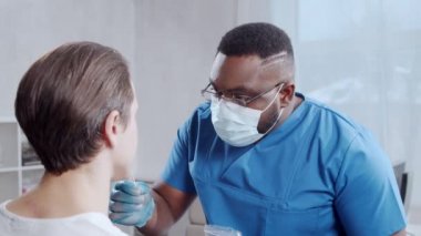 Afro-Amerikalı doktor koronavirüs testi yapıyor. Hastane ofisinde sağlık çalışanı ve hasta var. Covid-19 test ve güvenlik konsepti.