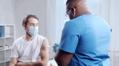 Afro-Amerikalı doktor şırınga ve şırınga kullanarak koronavirüs aşısı yapıyor. Hastane ofisinde sağlık çalışanı ve hasta var. Aşı ve güvenlik kavramı.