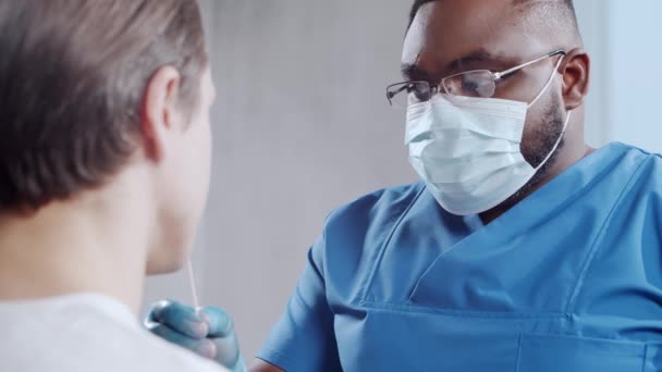 Afro-Amerikaanse dokter doet een coronavirustest. Medische medewerker en patiënt in het ziekenhuiskantoor. Covid-19 tests en veiligheidsconcept. — Stockvideo