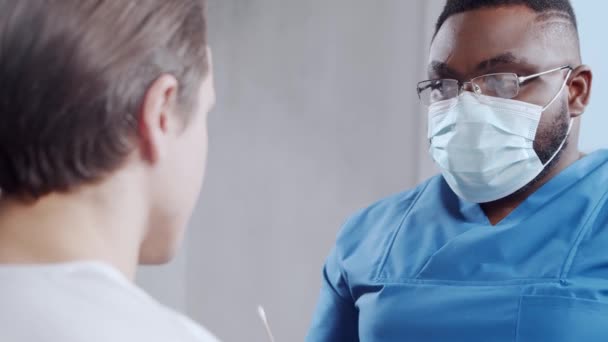 El médico afroamericano hace una prueba de coronavirus. Trabajador médico y paciente en la oficina del hospital. Ensayos Covid-19 y concepto de seguridad. — Vídeo de stock