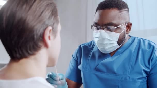 Afroamerikansk läkare gör ett coronavirus test. Läkare och patient på sjukhuskontoret. Covid-19 tester och säkerhetskoncept. — Stockvideo