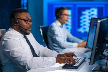 Çağrı merkezi çalışanı müşteriyle kulaklıkla konuşuyor. Afro-Amerikan destek operatörünün işyeri..