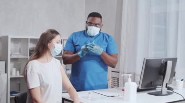 Afro-Amerikalı doktor şırınga ve şırınga kullanarak koronavirüs aşısı yapıyor. Hastane ofisinde sağlık çalışanı ve hasta var. Aşı ve güvenlik kavramı.