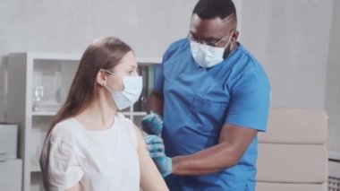 Afro-Amerikalı doktor şırınga ve şırınga kullanarak koronavirüs aşısı yapıyor. Hastane ofisinde sağlık çalışanı ve hasta var. Aşı ve güvenlik kavramı.