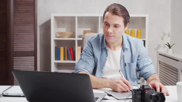 Freelance photographer workplace at home office. Young man works using computer, graphic tablet and camera. Remote job concept. — Stock Video