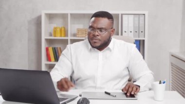 Ev ofisinde serbest tasarımcı işyeri. Genç Afro-Amerikalı bir adam bilgisayar ve grafik tableti kullanıyor. Uzak görev konsepti.