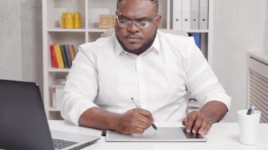 Ev ofisinde serbest tasarımcı işyeri. Genç Afro-Amerikalı bir adam bilgisayar ve grafik tableti kullanıyor. Uzak görev konsepti.