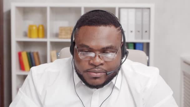 프리랜서의 직장. 아프리카계 미국인 남성은 컴퓨터와 헤드셋을 사용하여 가정 사무실에서 일 한다. 직원들이 회의 전화를 하고 있어요. 원격 직업 개념. — 비디오