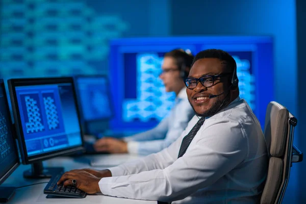 De medewerker van het callcenter spreekt met de klant per headset. Werkplaats van de Afrikaans-Amerikaanse hulpverlener. — Stockfoto