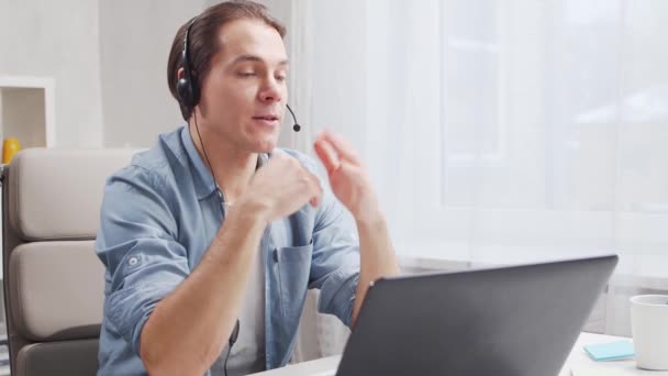 Local de trabalho do freelancer. Funcionário trabalha em casa usando computador e fone de ouvido. O jovem está a ter uma conferência. Conceito de trabalho remoto. — Vídeo de Stock