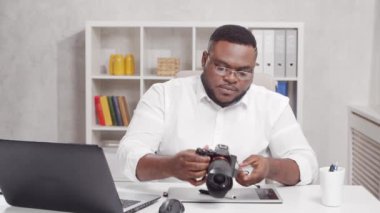 Ev ofisinde serbest fotoğrafçı işyeri. Genç Afro-Amerikalı adam bilgisayar, grafik tablet ve kamera kullanıyor. Uzak görev konsepti.