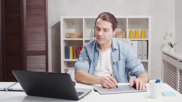 Lieu de travail de designer indépendant au bureau à la maison. Jeune homme travaille à l'aide d'un ordinateur et tablette graphique. Concept d'emploi à distance. — Video