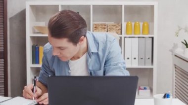 Ev ofisinden bağımsız çalışanların çalıştığı yer. Genç adam bilgisayar kullanıyor. Uzak görev konsepti.