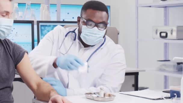 Afro-Amerikaanse arts maakt een coronavirusvaccin met een spuit en een injectienaald. Medische medewerker en patiënt in het ziekenhuiskantoor. Vaccinatie- en veiligheidsconcept. — Stockvideo