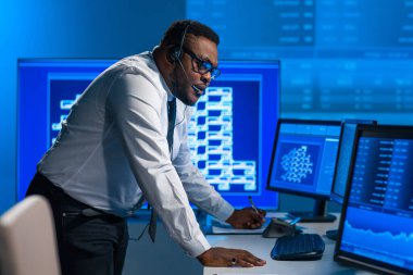 Afro-Amerikalı borsacı, çalışma istasyonu ve analiz teknolojisi kullanarak ofiste çalışıyor. Profesyonel tüccarların işyeri. Küresel finans piyasaları, iş dünyası, döviz kurları ve bankacılık kavramları.