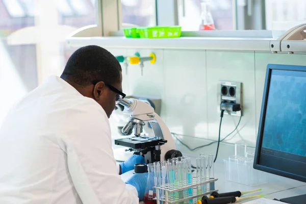 Afrikai-amerikai férfi, aki laborban dolgozik. A tudós orvos orvosi kutatást végez. Laboratóriumi eszközök: mikroszkóp, kémcsövek, berendezések. Biotechnológia, kémia, tudomány, kísérletek és egészségügy. — Stock Fotó