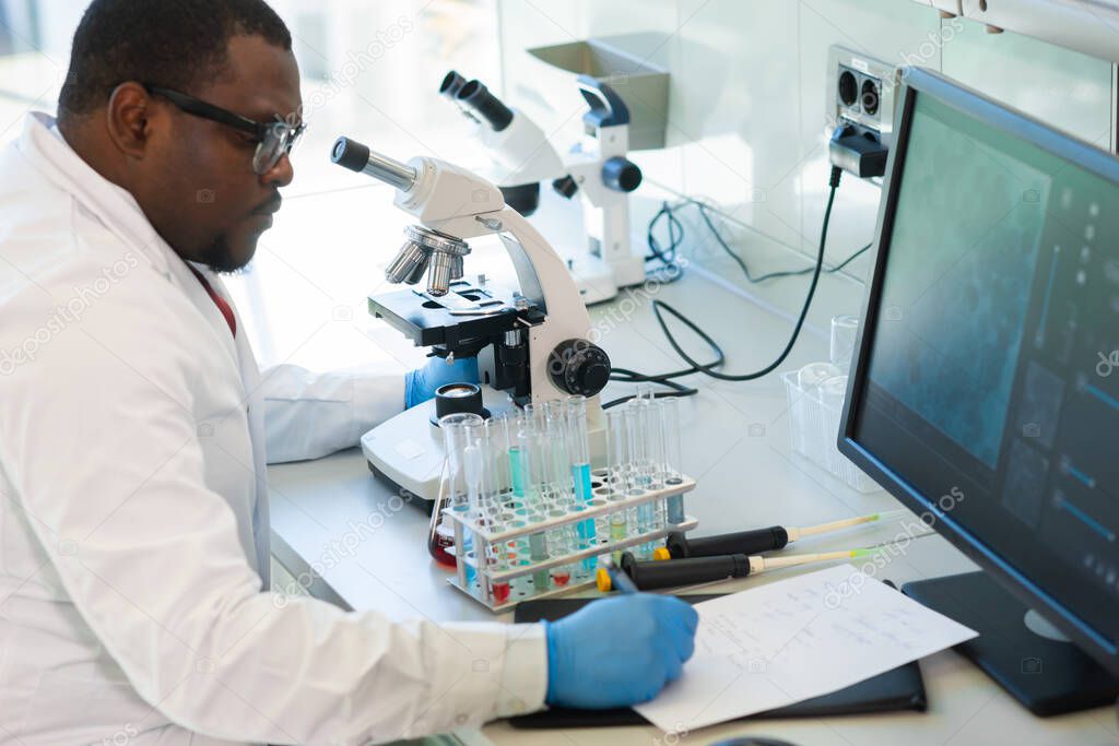 African-american scientist working in lab. Doctor making microbiology research. Laboratory tools: microscope, test tubes, equipment. Biotechnology, chemistry, bacteriology, virology and health care.