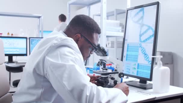 Científico profesional afroamericano está trabajando en una vacuna en un moderno laboratorio de investigación científica. Trabajo de ingeniero genético. Tecnología futurista y concepto de ciencia. — Vídeo de stock