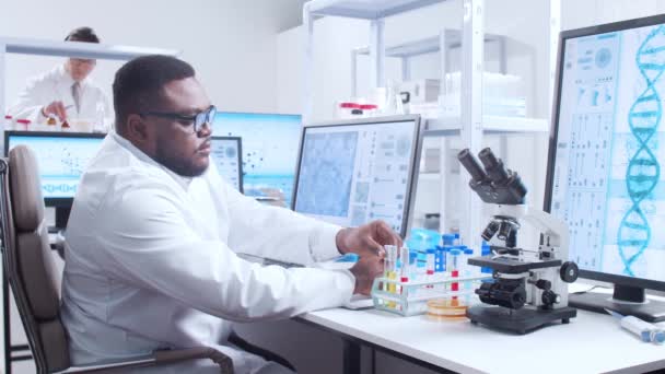Profesyonel Afro-Amerikan bilim adamı modern bir bilimsel araştırma laboratuvarında aşı üzerinde çalışıyor. Genetik mühendisliği işyeri. Fütürist teknoloji ve bilim konsepti. — Stok video
