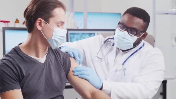 Afro-Amerikaanse arts maakt een coronavirusvaccin met een spuit en een injectienaald. Medische medewerker en patiënt in het ziekenhuiskantoor. Vaccinatie- en veiligheidsconcept. — Stockvideo
