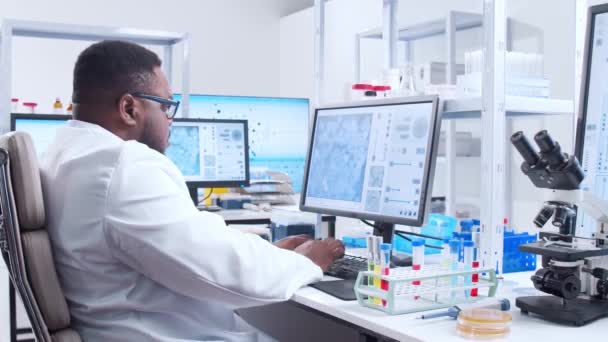 Professionele Afro-Amerikaanse wetenschapper werkt aan een vaccin in een modern wetenschappelijk onderzoekslaboratorium. Genetische ingenieur werkplek. Futuristische technologie en wetenschapsconcept. — Stockvideo