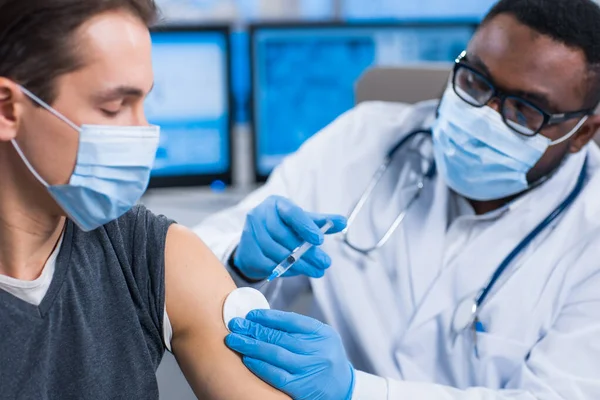 Afroamerykanin wytwarza szczepionkę przeciw koronawirusowi używając strzykawki i igły podskórnej. Profesjonalny pracownik medyczny i pacjent w biurze szpitalnym. Szczepienie i bezpieczeństwo. — Zdjęcie stockowe
