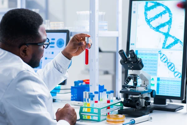 Επαγγελματίας Αφρο-Αμερικανός επιστήμονας εργάζεται πάνω σε ένα εμβόλιο σε ένα σύγχρονο εργαστήριο επιστημονικής έρευνας. Στο χώρο εργασίας των γενετιστών. Μελλοντική τεχνολογία και επιστήμη. — Φωτογραφία Αρχείου