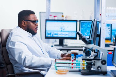 Profesyonel Afro-Amerikan bilim adamı modern bir bilimsel araştırma laboratuvarında aşı üzerinde çalışıyor. Genetik mühendisliği işyeri. Gelecekteki teknoloji ve bilim.