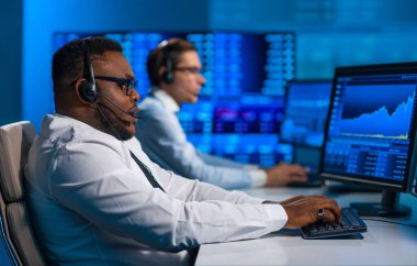 Komisyonculardan oluşan bir ekip, çalışma istasyonu ve analiz teknolojisini kullanarak ofiste çalışıyor. Profesyonel tüccarların işyeri. Küresel finans piyasaları, iş dünyası, döviz kurları ve bankacılık kavramları.