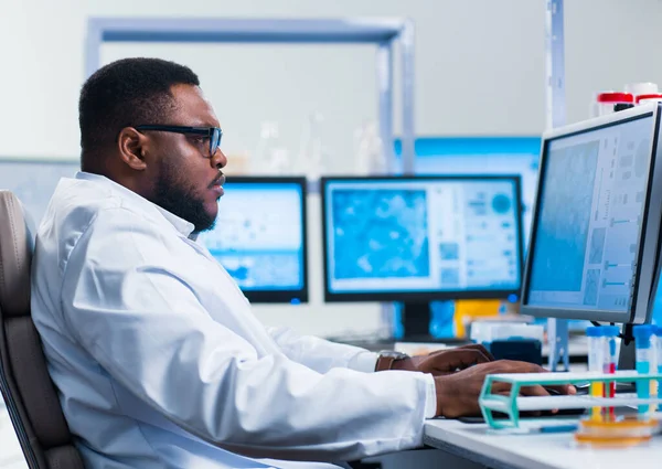 Επαγγελματίας Αφρο-Αμερικανός επιστήμονας εργάζεται πάνω σε ένα εμβόλιο σε ένα σύγχρονο εργαστήριο επιστημονικής έρευνας. Στο χώρο εργασίας των γενετιστών. Μελλοντική τεχνολογία και επιστήμη. — Φωτογραφία Αρχείου