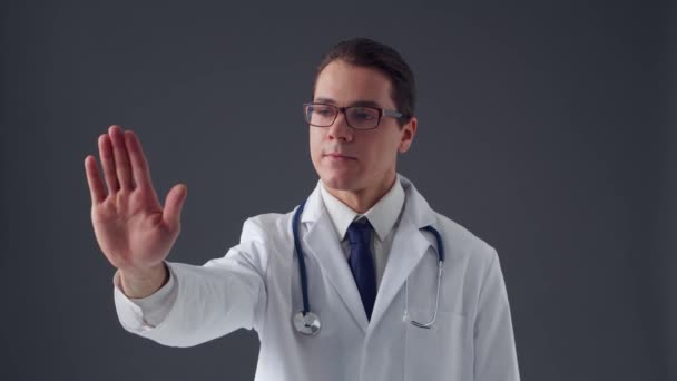 Retrato de estudio de un joven médico profesional que trabaja con interfaces digitales de imágenes invisibles sobre fondo gris — Vídeos de Stock