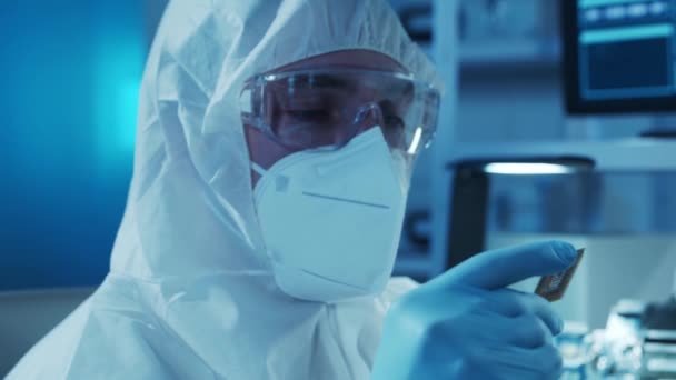 Microelectronics engineer works in a modern scientific laboratory on computing systems. Electronic factory worker in a protective suit is looking on the microprocessor. — Stock Video