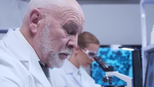 Oudere hoogleraar en jonge laboratoriumassistent doen wetenschappelijk experiment in een modern laboratorium. Genetische ingenieurs werkplek. Het concept van wetenschap, geneeskunde en vaccinontwikkeling. — Stockvideo