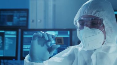 Mikro elektronik mühendisi, bilgisayar sistemleri üzerine modern bir bilim laboratuvarında çalışıyor. Koruyucu giysili bir fabrika işçisi mikroişlemciye bakıyor..